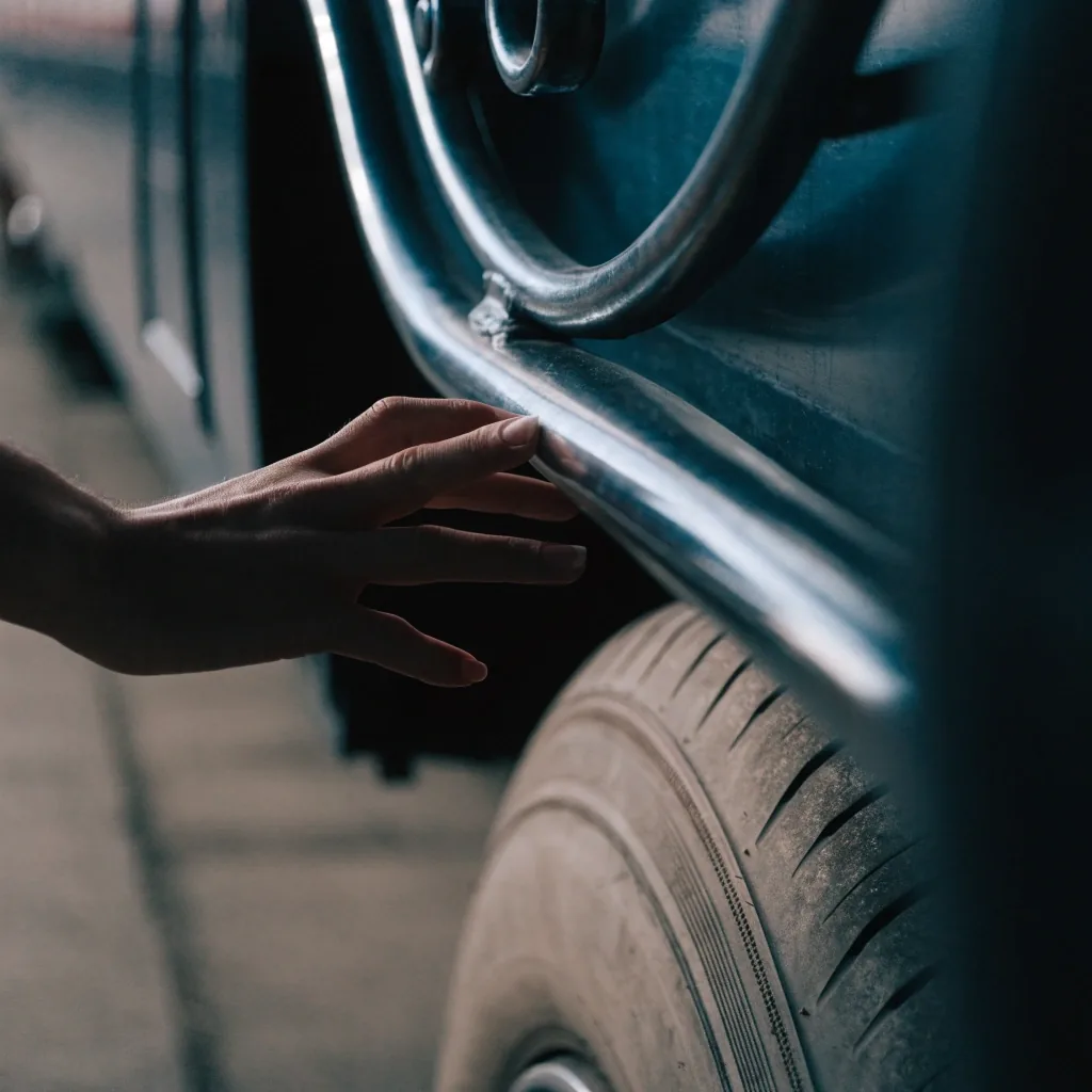 Close detail of a traveller's hand holding a plain blank boarding slip beside a coach wheel arch in single cold side light